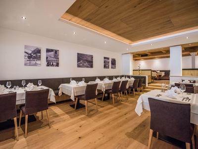 Modernes Restaurant mit Holzboden, weißen Tischdecken und braunen Stühlen in hellen Räumen.