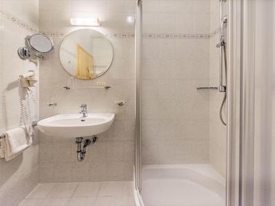 Helles Badezimmer mit runder Spiegel, weißem Waschbecken und Glastür-Dusche in neutralen Tönen.