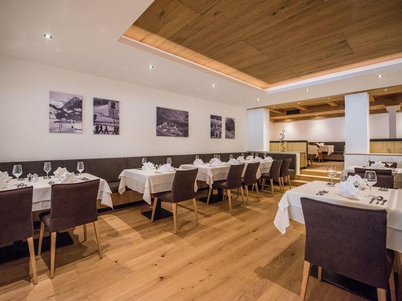 Modernes Restaurant mit Holzboden, weißen Tischdecken und braunen Stühlen in hellen Räumen.