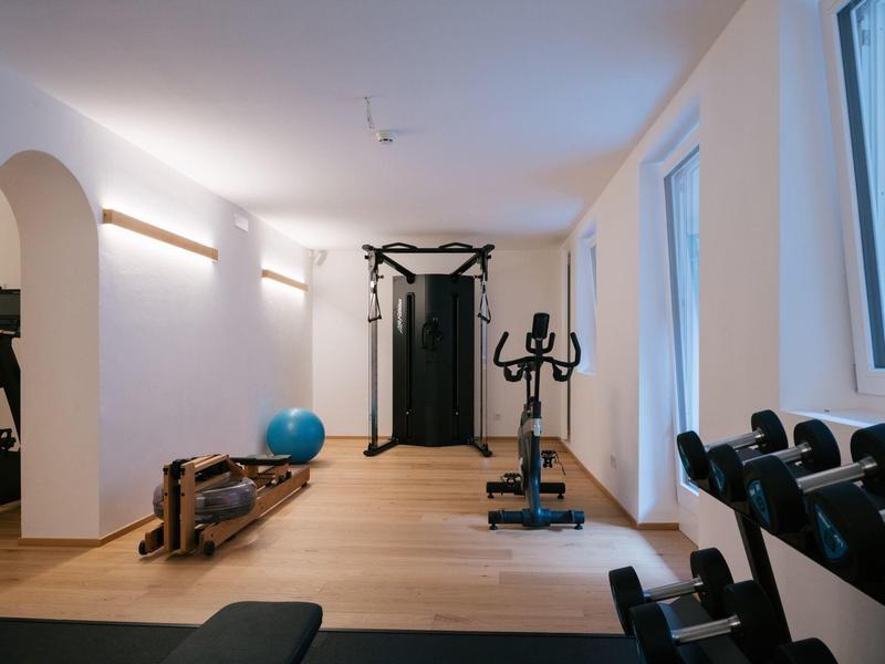 Helles, modernes Fitnesszimmer mit Holzfußboden, Trainingsgeräten und großen Fenstern.