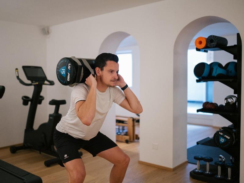 Mann in Sportkleidung macht Kniebeuge mit Kettlebell in hellem Fitnessraum.