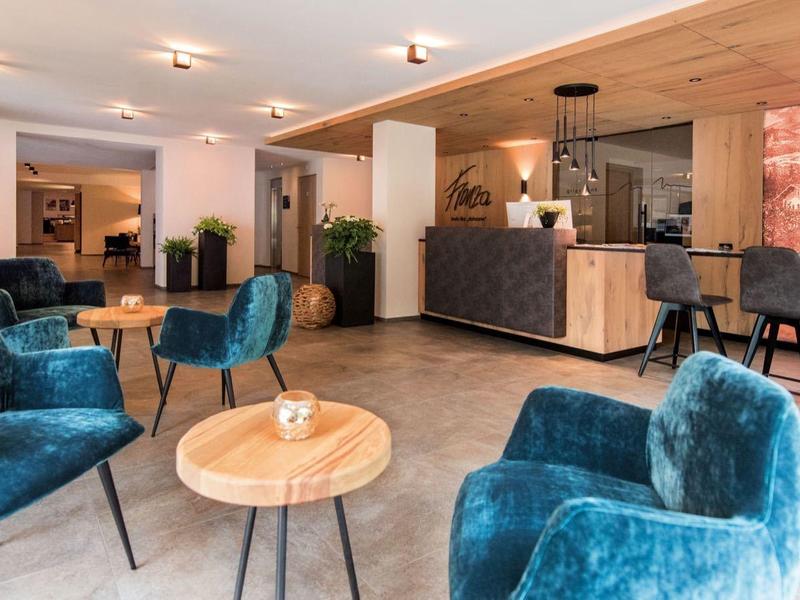 Moderner Lounge-Bereich mit blauen Samtstühlen, Holzplatten, runden Tischen und heller Raumgestaltung.