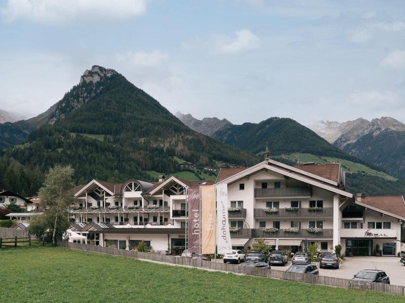 Mehrstöckige Häuser vor grünen Bergen unter blauem Himmel mit leicht bewölkten Wolken.