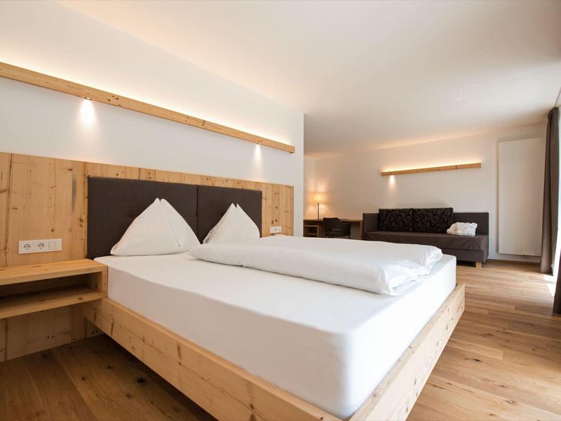 Helles Schlafzimmer mit Holzmöbeln, großem Bett, Sofa und indirekter Beleuchtung an der Wand.
