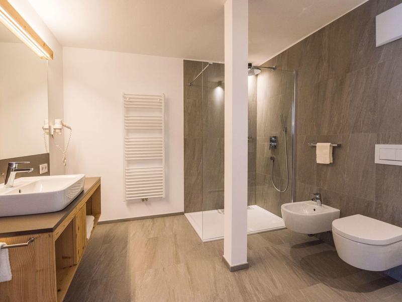 Modernes Badezimmer mit Holzfußboden, großer Dusche, Wand-WC und Bidet, hellen Wänden und Warmlicht.