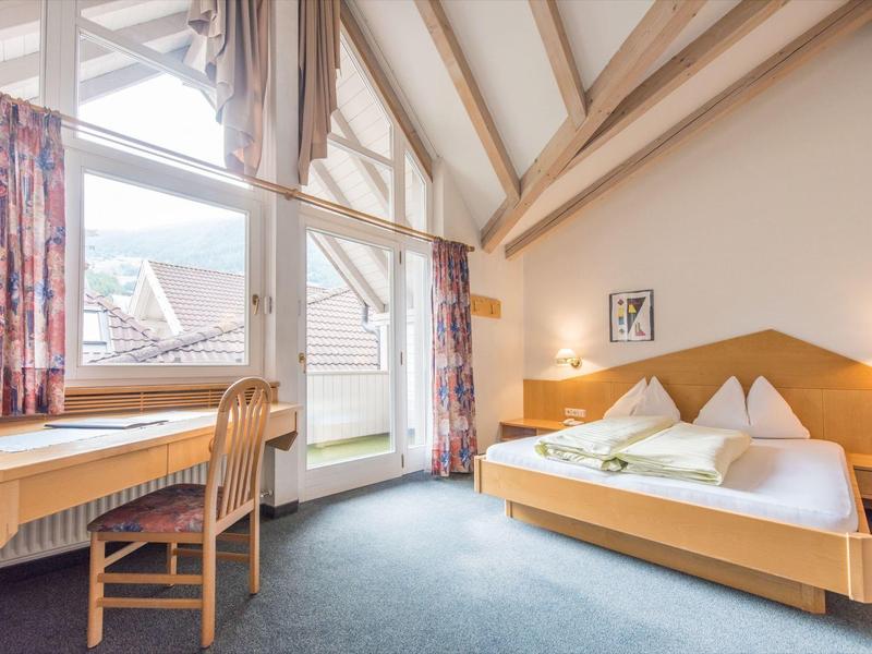 Helles Schlafzimmer mit Holzmöbeln, großem Bett, Schreibtisch, Balkon und großen Fenstern.