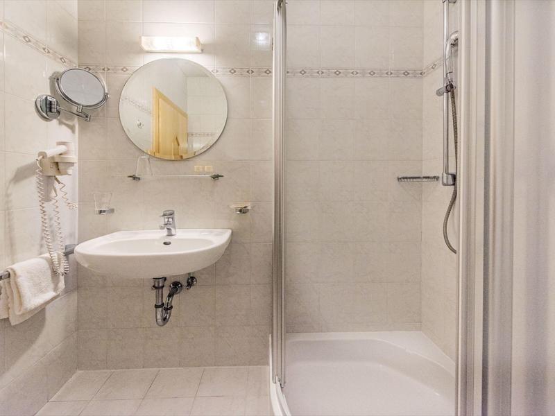 Helles Badezimmer mit runder Spiegel, weißem Waschbecken und Glastür-Dusche in neutralen Tönen.