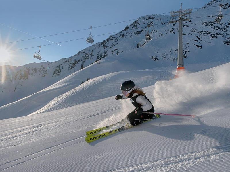 Kind fährt Ski im Schneehang bei sonnigem Winterwetter mit Sesselliften im Hintergrund.