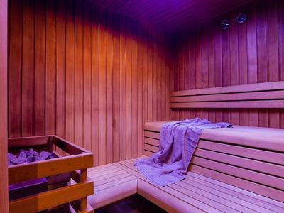 Holzsauna mit Bank, Saunaofen und einem lila Handtuch, warme rote Beleuchtung innen.