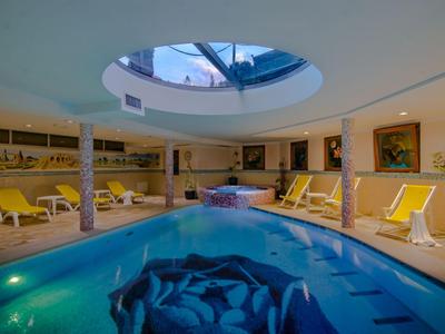 Binnen wellnessruimte met zwembad, bubbelbad en ligstoelen onder een glazen plafond.