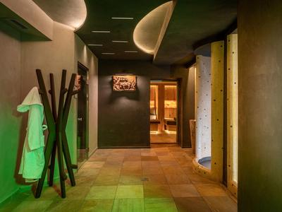 Ein schmaler Flur mit warmen, gedämpften Lichtquellen und braunen Wänden, Robe hängt an Ständer.