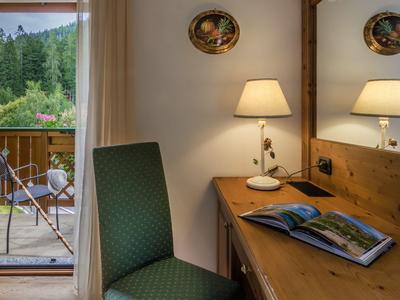 Gemütlicher Raum mit grünem Stuhl, Holztisch, Lampe und Blick auf Balkon mit Stühlen und Wald.
