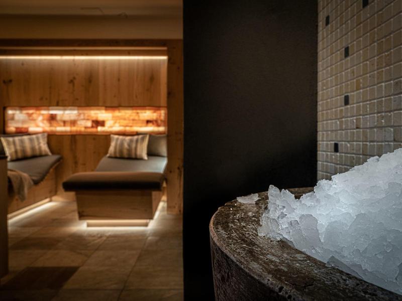 Gemütliche Sauna mit Holzbänken, Kissen und einem Eimer voller Eiswürfel im Vordergrund.