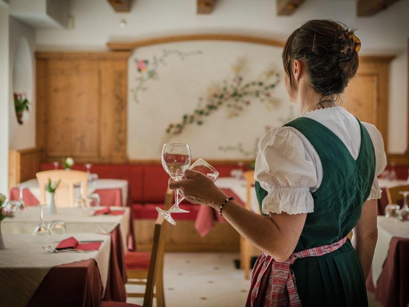 Frau in Dirndl hält Weinglas in rustikalem Gastraum mit Holz und roten Polstern.