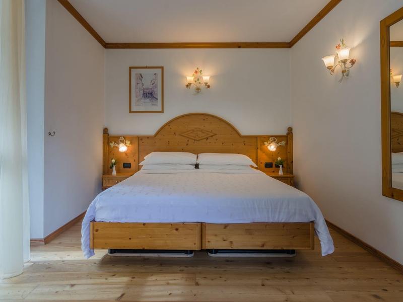 Hell eingerichtetes Schlafzimmer mit Holzbett, weißer Bettwäsche und Wandlampen neben Gemälde.