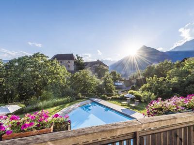Schwimmbad mit Blumen, Bäumen und Bergen bei sonnigem Wetter, Blick von einem Holzgeländer.