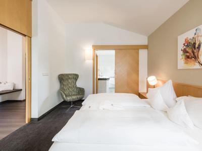 Klassisches Schlafzimmer mit zwei weißen Betten, grünem Sessel und hellem Holzmöbel.