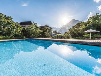 Piscina blu con acqua limpida circondata da alberi e un ombrellone sotto un cielo soleggiato.
