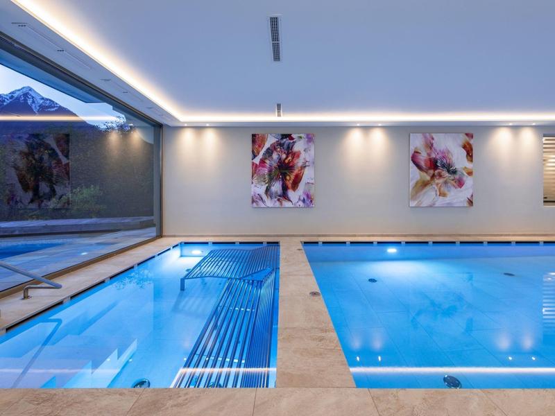Innenraum mit zwei blauen Schwimmbecken, Wandkunst und großen Fenstern mit Bergblick.