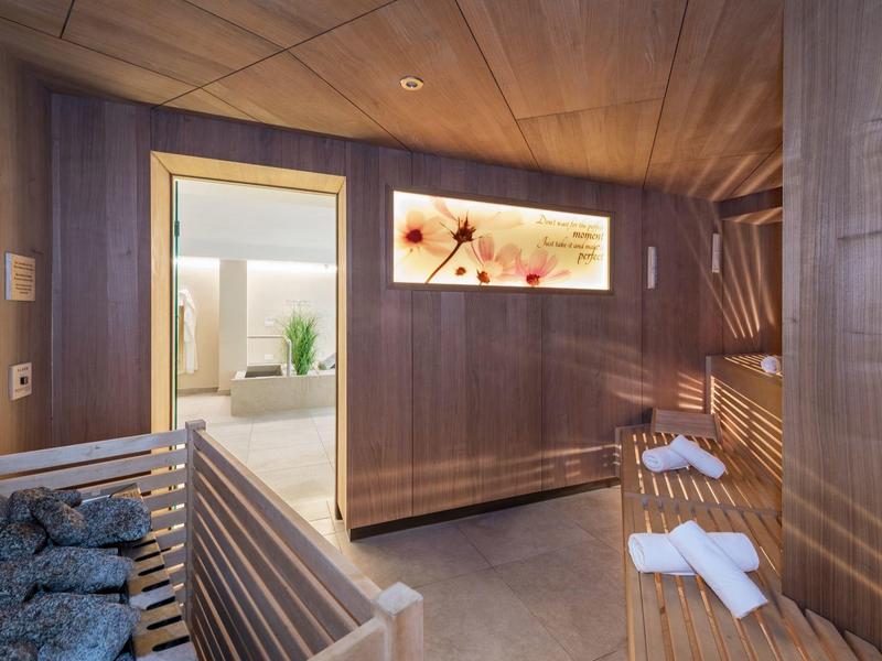 Moderne Sauna mit Holzverkleidung, Bänken, Handtüchern und Blick in angrenzenden Raum.