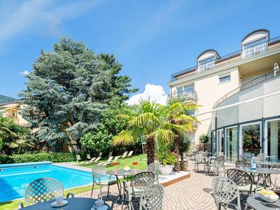 Moderner Garten mit blauem Pool, Palme, Sonnenliegen und Terrasse an hellem Haus bei klarem Himmel.