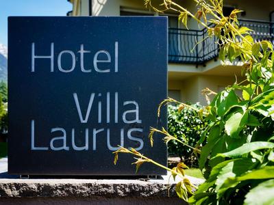 Schild mit der Aufschrift ‚Hotel Villa Laurus‘ vor einem Hotelgebäude und grüner Vegetation