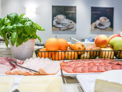 Küche mit frischem Obst, Kräutertopf, Aufschnitt und Käse auf einem weißen Tisch.