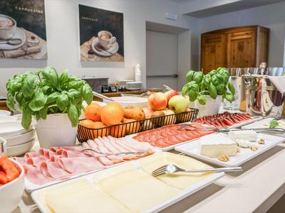 Buffet mit Aufschnitt, Käse, Tomaten, frischen Kräutern und Obst in heller, moderner Küche.