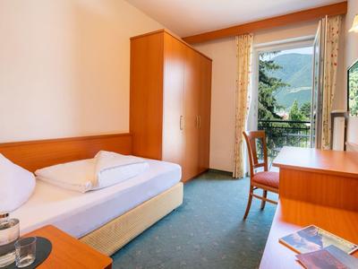 Kleines Schlafzimmer mit Einzelbett, Holzmöbeln, grünem Teppich und Fenster mit Blick ins Grüne.