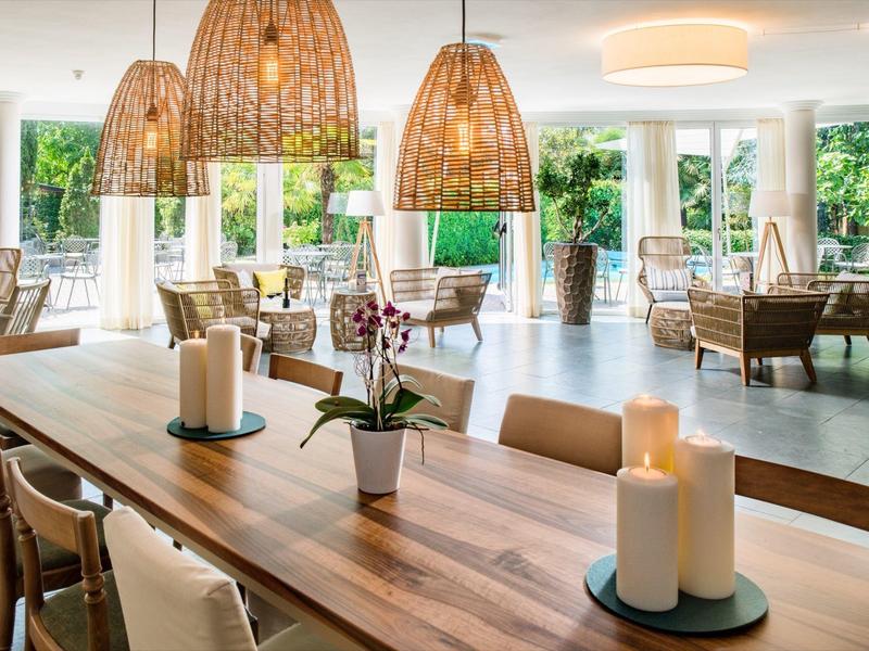 Modernes Esszimmer mit hölzernem Tisch, Stühlen, drei geflochtenen Lampen und großen Fenstern.