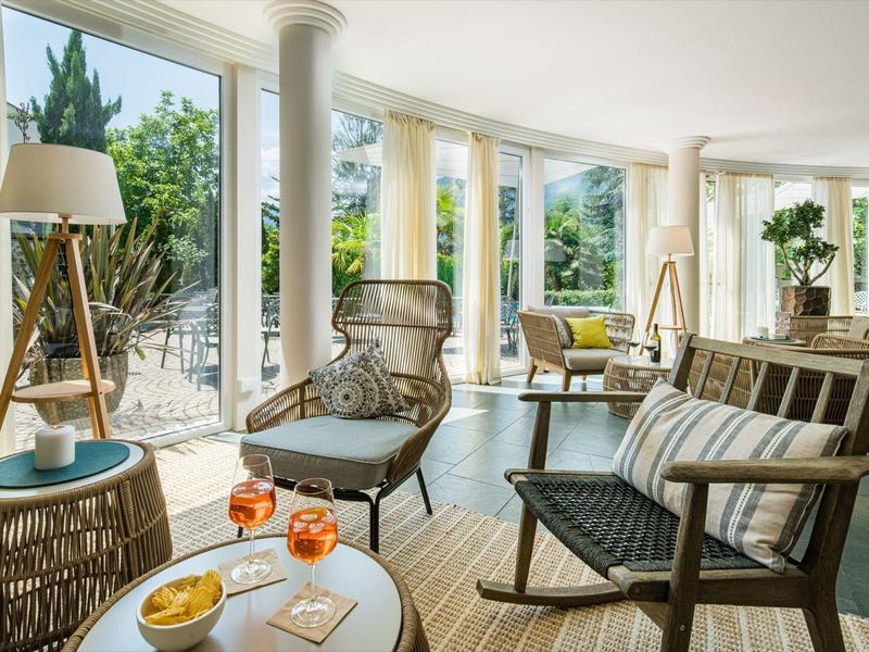 Heller Wohnzimmerbereich mit großen Fenstern, Holzstuhl, Couchtisch und gemütlichen Sitzplätzen.