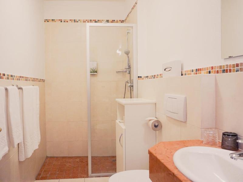 Helles Badezimmer mit Duschkabine, Waschbecken, Handtuchhalter und weiß-roten Fliesenakzenten.