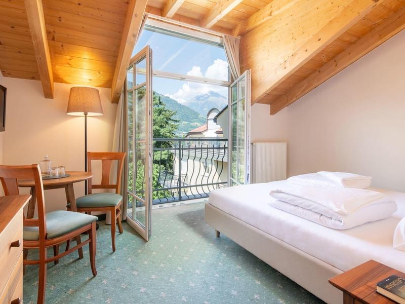 Gemütliches Schlafzimmer mit Holzbalken, Doppelbett, Balkon und Blick auf Berge und Himmel.