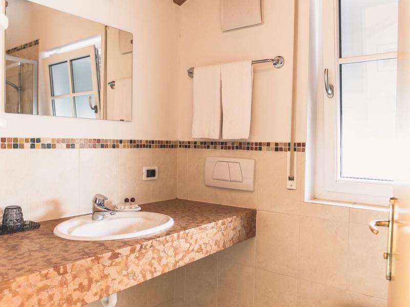 Helles Badezimmer mit Mosaik-Waschbeckenplatte, rechteckigem Spiegel, Handtüchern und Fenster.