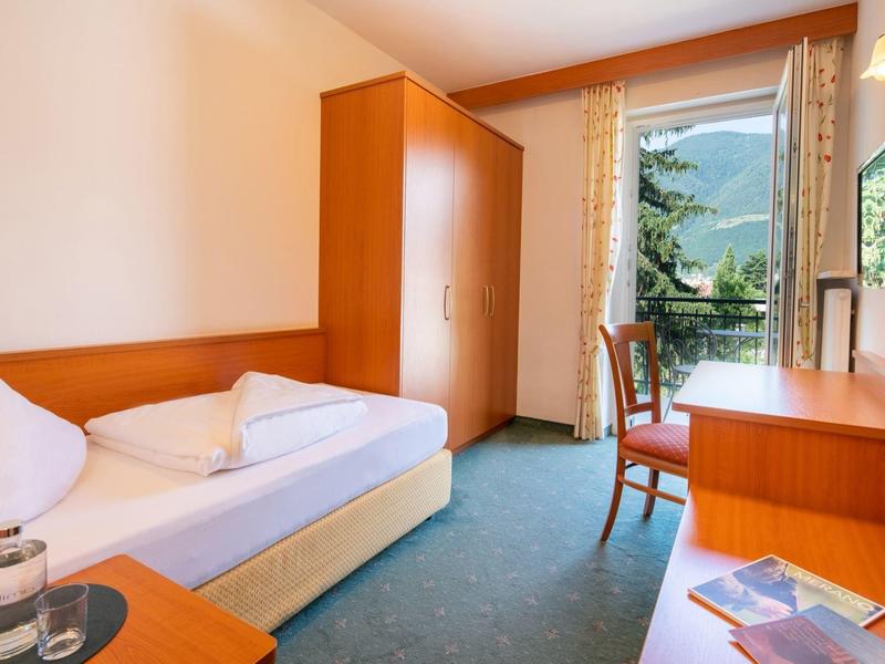 Kleines Schlafzimmer mit Einzelbett, Holzmöbeln, grünem Teppich und Fenster mit Blick ins Grüne.