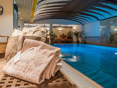 Innenbereich mit blau beleuchtetem Schwimmbad, Holzdecke und gefalteten Handtüchern im Vordergrund.