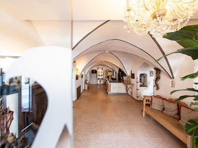 Heller, langer Flur mit gewölbter Decke, Holzbank, Pflanzen und Kronleuchter in warmem Licht.