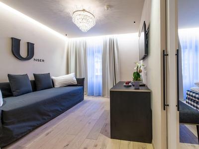 Moderner Wohnraum mit grauer Couch, Holzboden, Vorhängen und beleuchtetem Kronleuchter.