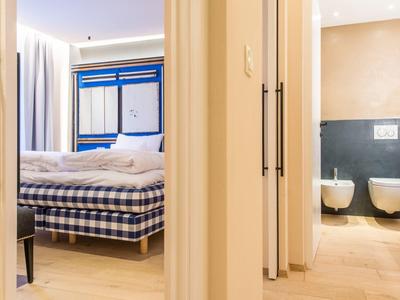 Helles Schlafzimmer mit kariertem Bett und angrenzendem Bad mit WC und Bidet, beige Fliesen.