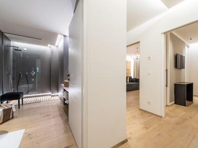 Moderner Hotelflur mit Holzboden, weißen Wänden, Spiegel, Beleuchtung und einzelnen Möbelstücken.