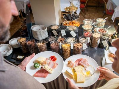Zwei Personen wählen aus einer vielfältigen Frühstücksbuffet-Auslage mit Müsli, Käse und Aufschnitt.