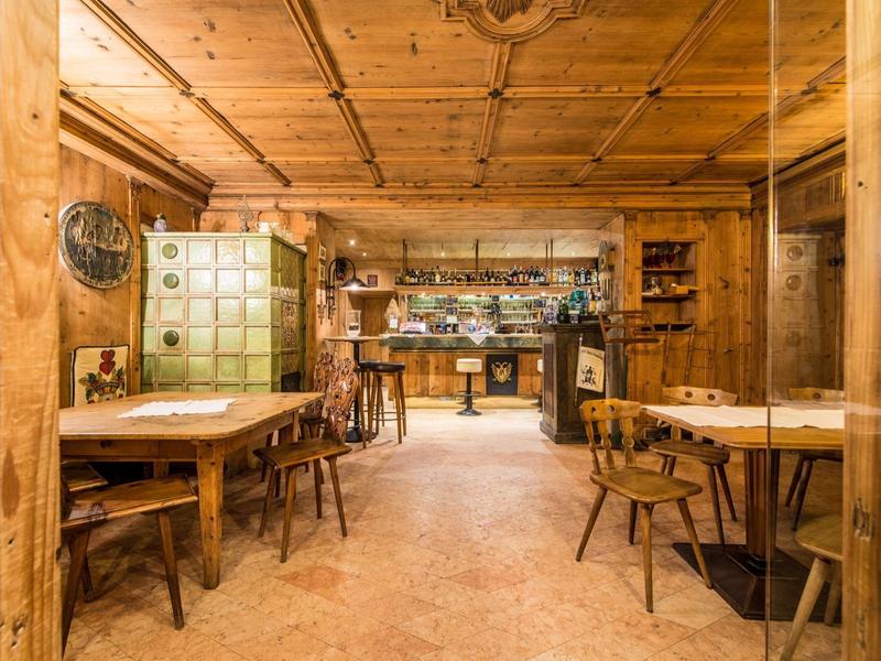 Rustikaler Gastraum mit Holztischen, Stühlen, grüner Kachelofen und Holzdecke.