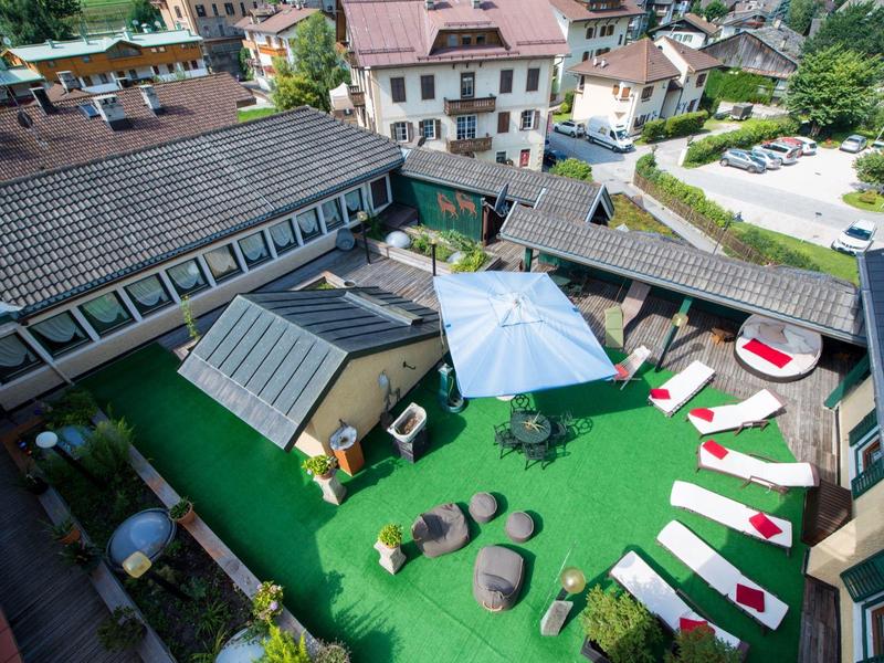 Dachterrasse mit grünem Kunstrasen, weißen Liegen, runden Sitzkissen und großen Sonnenschirmen.