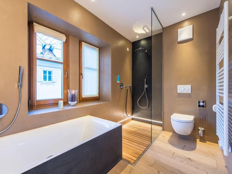 Modernes Badezimmer mit Badewanne, Regendusche, Toilette und Holzfußboden, in warmen Farben gestaltet.