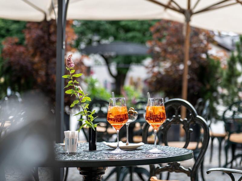 Tisch mit zwei Aperol-Spritz in eleganter Außenbereich-Café-Atmosphäre unter Sonnenschirm.