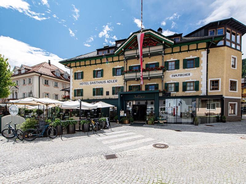Gelbes, dreistöckiges Gebäude mit Außenbestuhlung und Bayerischer Flagge unter blauem Himmel.