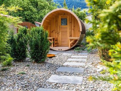 Runder Holz-Gartenpavillon mit kleinem Fenster, umgeben von Kies und grünen Pflanzen.