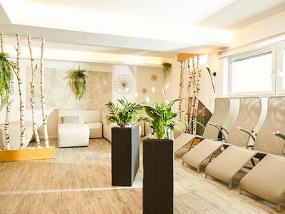 Heller Wellnessraum mit bequemen Liegen, weißen Holzdetails und grünen Pflanzen in modernen Pflanzgefäßen.