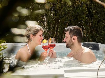 Junges Paar entspannt im Whirlpool und stößt mit bunten Cocktails an.