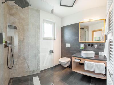 Modernes Badezimmer mit großer Dusche, weißer Toilette, Waschbecken auf Holzwaschtisch und Spiegel.